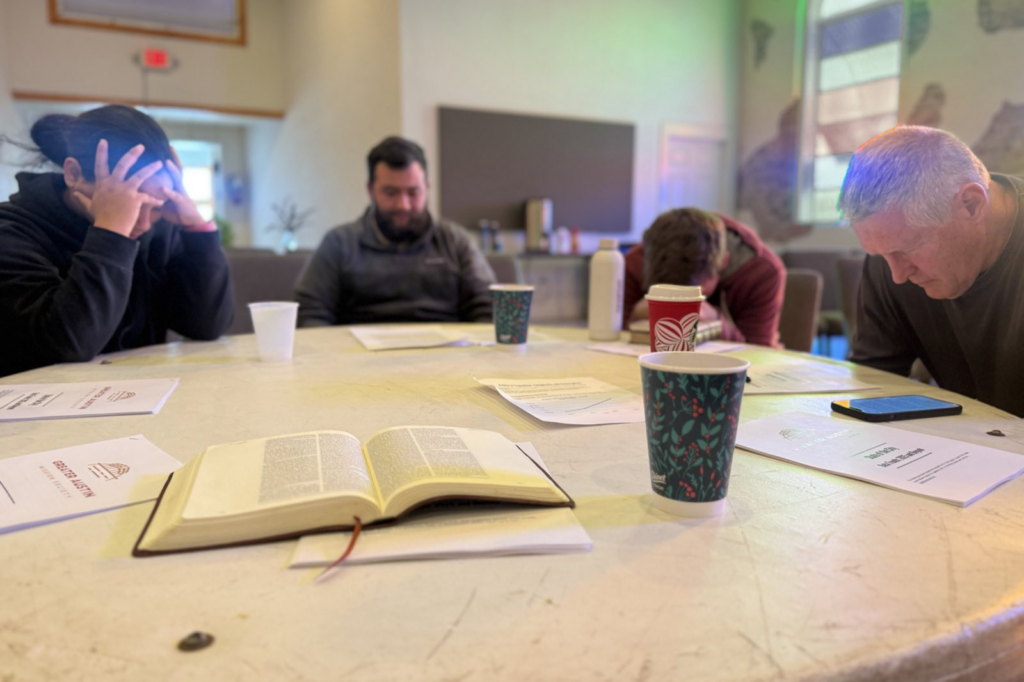 An open Bible rests on a table as participants pray together at a Greater Austin Mission Society gathering.
